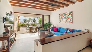 A modern living room with a wooden ceiling, a blue sofa, a TV, and a dining area with a table and chairs. - Stylish 3BR Villa I Pool & Sunset Views (Zihuatanejo)