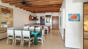 A modern kitchen with wooden beams, a dining area with white chairs, and a painting of a turtle on the wall. - Stylish 3BR Villa I Pool & Sunset Views (Zihuatanejo)