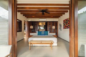 A bedroom with a bed, a bench, wooden beams, a ceiling fan, and a colorful artwork on the wall. - Stylish 3BR Villa I Pool & Sunset Views (Zihuatanejo)