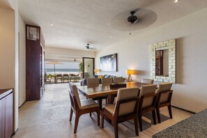 Un comedor con una mesa grande y sillas, un ventilador de techo y vista al océano.