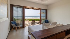 A bedroom with a large bed, a wooden desk, and a view of the beach through open sliding doors.