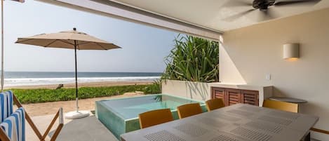 A poolside dining area with a view of the ocean, a ceiling fan, and a table with chairs.