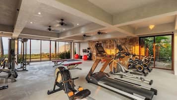 A gym with various exercise equipment, large windows, and a stone wall.