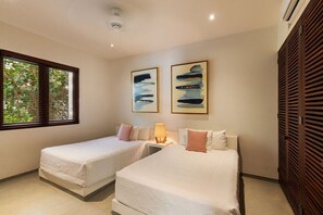 A hotel room with two beds, a window with blinds, and artwork on the wall.