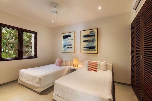 A hotel room with two beds, a window with blinds, and artwork on the wall.