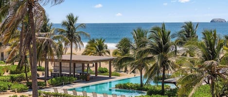 A resort with a pool, palm trees, and a view of the ocean.