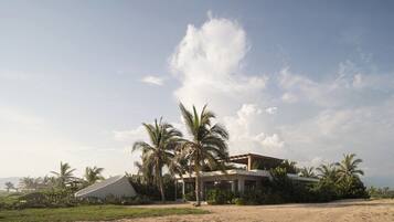 A modern building with a flat roof, surrounded by palm trees and a clear sky.