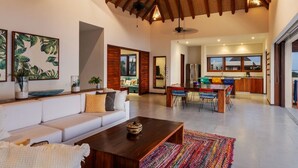 A spacious living area with a high ceiling, a dining area, and a kitchen visible through an open doorway.
