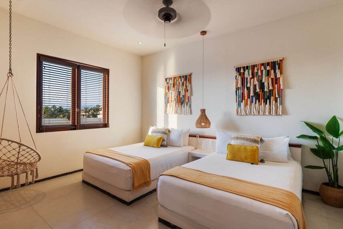 Habitación de hotel con dos camas, una silla colgante, un ventanal grande y una obra de arte en la pared.