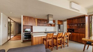 A modern kitchen with wooden cabinets, a central island with chairs, and a dining area.