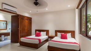 A hotel room with two beds, a wooden wardrobe, a bathroom with a mirror, and an air conditioning unit.