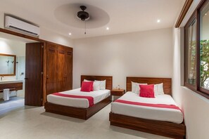 Habitació d'hotel amb dos llits, un armari de fusta, un bany amb mirall i un aire condicionat.