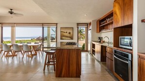 A modern kitchen with a large island, wooden cabinets, and a view of the beach. - 3BR Beachfront Villa • Private Terrace + Pool (Zihuatanejo)