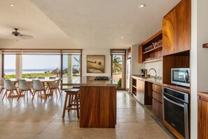 A modern kitchen with a large island, wooden cabinets, and a view of the beach. - 3BR Beachfront Villa • Private Terrace + Pool (Zihuatanejo)