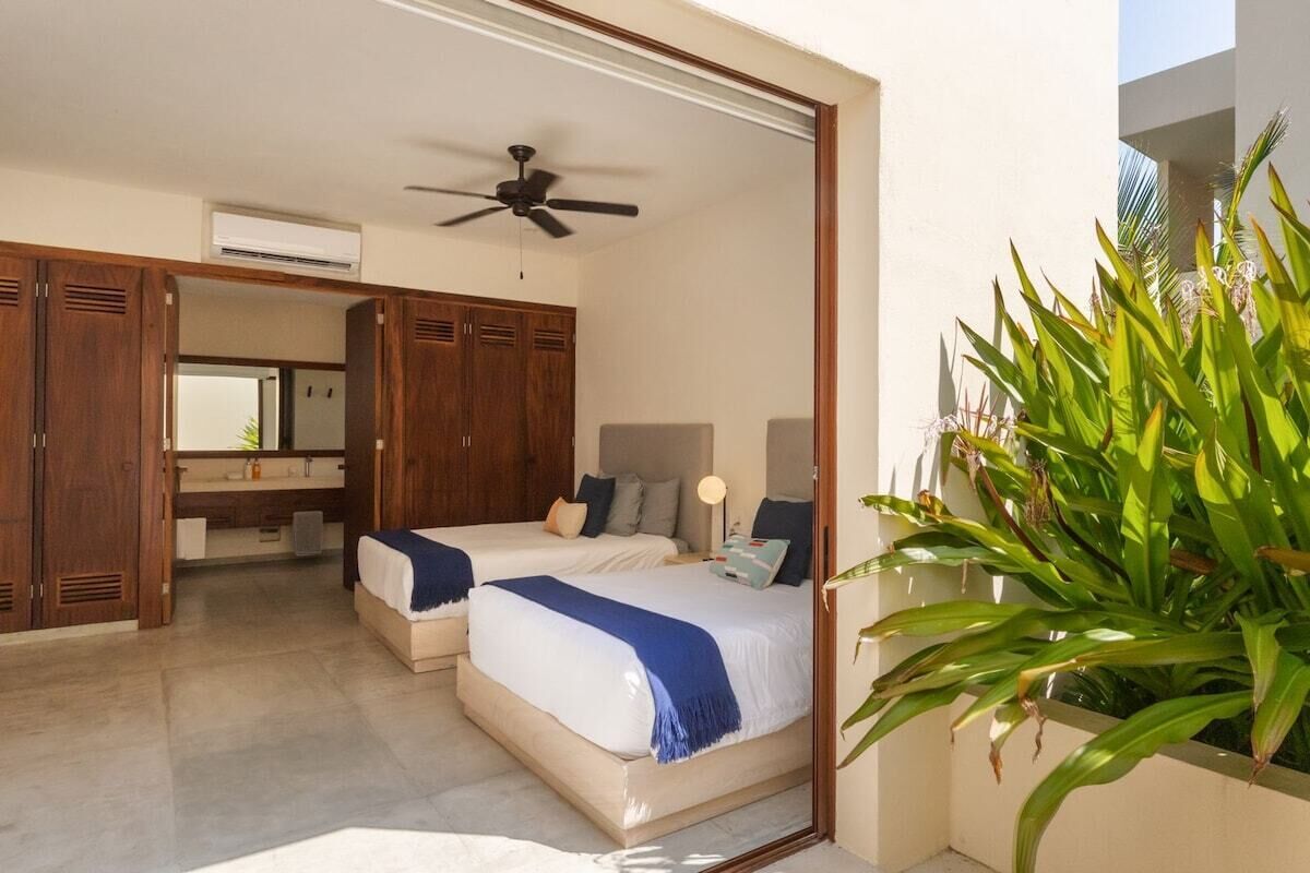Een slaapkamer met twee bedden, een plafondventilator, een grote spiegel en een potplant.