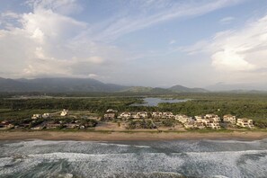 Een kustresort met strandvilla's, een strand en een bergachtige achtergrond.