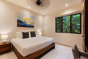 A bedroom with a large bed, a painting on the wall, a window with a view of trees, and a chair.