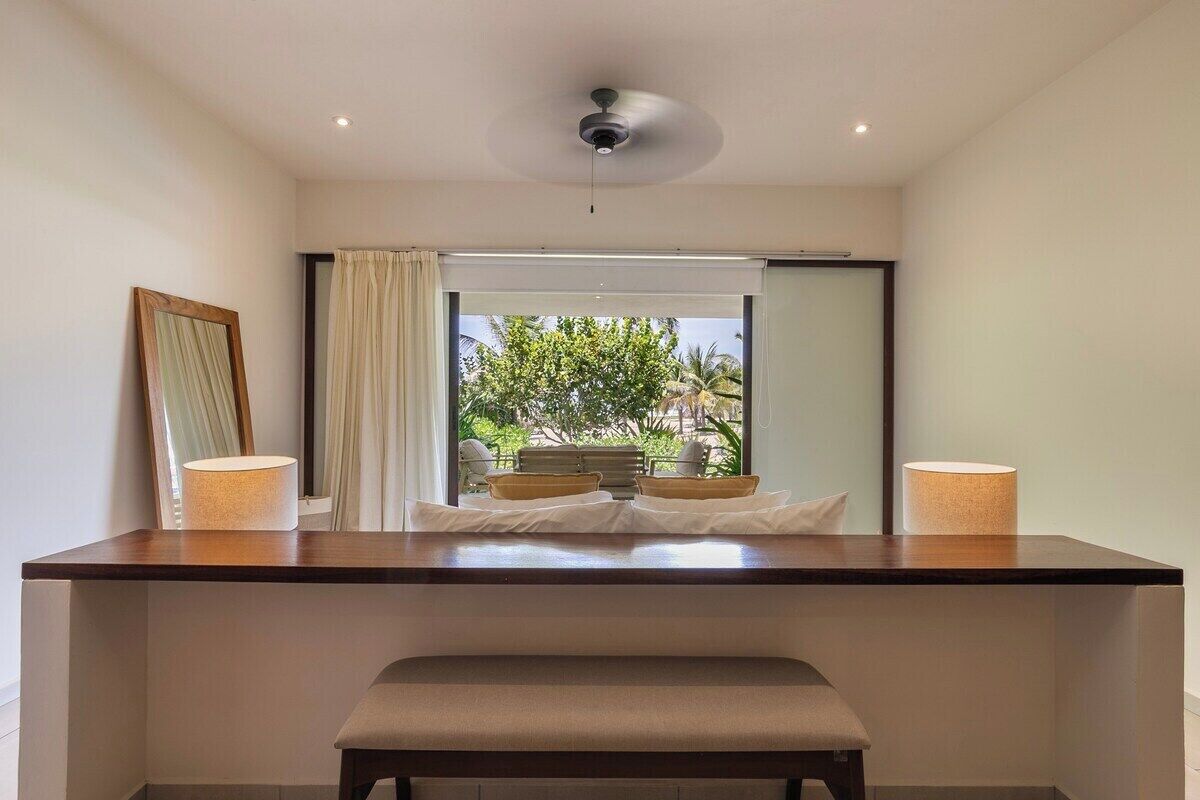 Une salle de bain moderne avec un grand miroir, un banc et une vue sur un espace extérieur tropical.