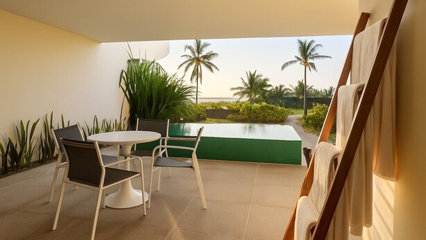 Ein moderner Außenbereich mit Sitzgelegenheit, Tisch und Stühlen, einer grünen Wand und Blick auf Palmen und einen Pool.
