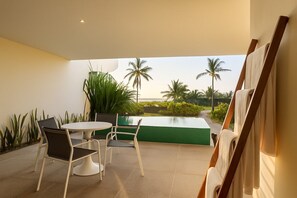 A modern outdoor seating area with a table and chairs, a green wall, and a view of palm trees and a pool.