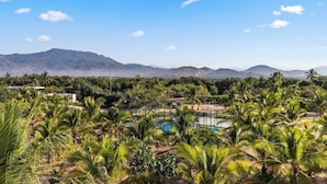 A landscape with palm trees, a swimming pool, and distant mountains.
