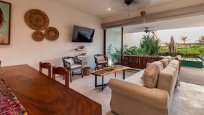 A modern living room with a wooden dining table, sofas, a flat-screen TV, and a balcony with plants.