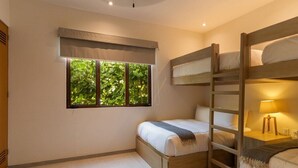 Una camera da letto con un letto a castello, un letto singolo, una finestra vista verde e un comodino con una lampada.