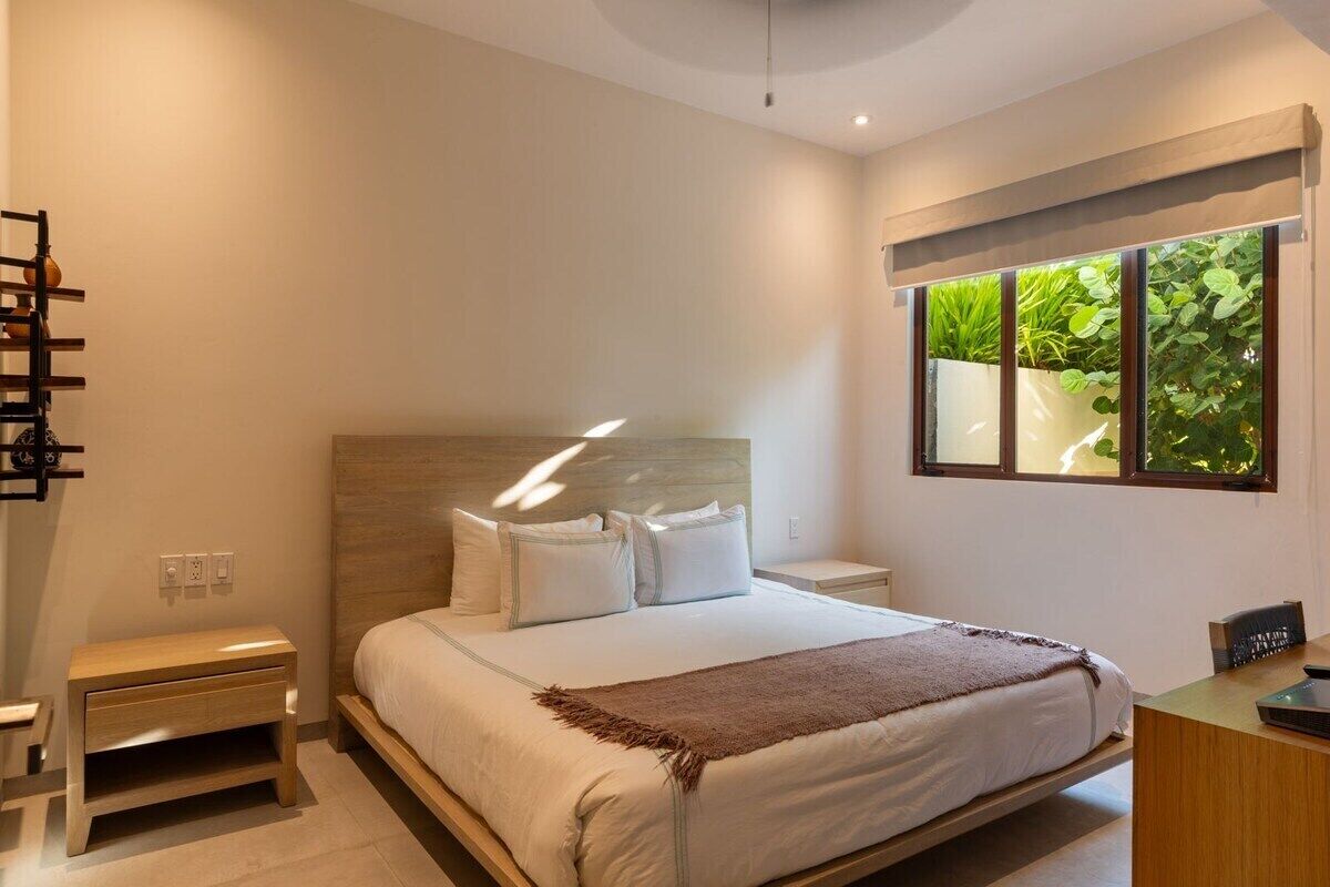 Une chambre à coucher moderne, avec un lit, des tables de chevet, une commode et une fenêtre donnant sur un paysage verdoyant.