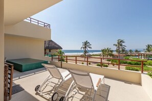A balcony with a view of the beach, lounge chairs, and a thatched-roof structure. - 2BR Boho Apartment • Ocean View Stay in Zihua (Zihuatanejo)
