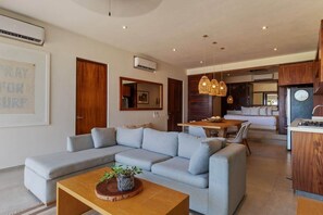 A modern living room with a sectional sofa, a wooden coffee table, and a dining area with a wooden table and chairs. - 2BR Boho Apartment • Ocean View Stay in Zihua (Zihuatanejo)