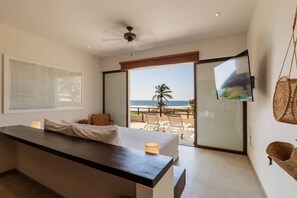 A modern bedroom with a large bed, a TV mounted on the wall, and a balcony with a view of the beach. - 2BR Boho Apartment • Ocean View Stay in Zihua (Zihuatanejo)