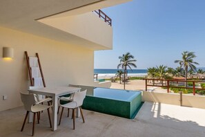 A balcony with a view of the ocean, a pool, and a dining area with chairs and a table. - 2BR Boho Apartment • Ocean View Stay in Zihua (Zihuatanejo)