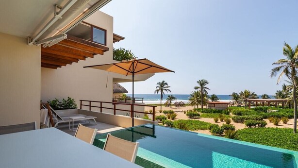 Ein Pool ohne Ende mit Blick auf den Strand, Sitzgelegenheiten im Freien und ein überdachter Bereich mit Tisch und Stühlen.