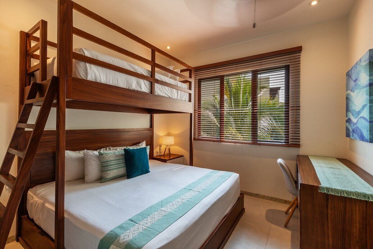 Une chambre avec un lit superposé, un bureau et une fenêtre avec des stores.