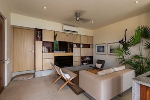 A modern living room with a sofa, a small table, and a bench. There is a bookshelf with various items and a ceiling fan.