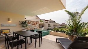 Une terrasse extérieure avec une table et des chaises, un fauteuil de relaxation, une petite piscine et un mur en pierre.