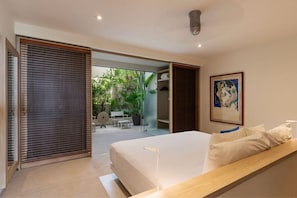 A modern bedroom with a large bed, a wooden bench, and a view of an outdoor garden. - Romantic 1BR Villa • Private Pool + Outdoor Shower (Zihuatanejo)