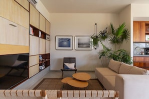 A living room with a sofa, a chair, a coffee table, and a bookshelf. There are two framed pictures on the wall.