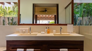 A bathroom with a large mirror, two sinks, wooden cabinets, and a ceiling fan. - 1BR Romantic Villa • Ocean View in Playa Blanca (Zihuatanejo)