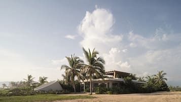 Un bâtiment moderne doté d’un toit plat, entouré de palmiers et surplombé d’un ciel dégagé.