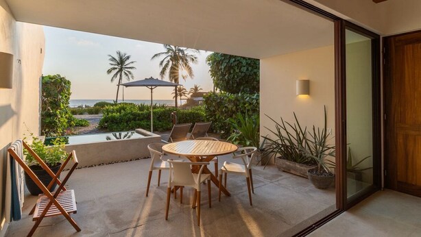A patio with a round table and chairs, a small pool, and a view of the ocean and palm trees. - 1BR Romantic Villa • Ocean View in Playa Blanca (Zihuatanejo)