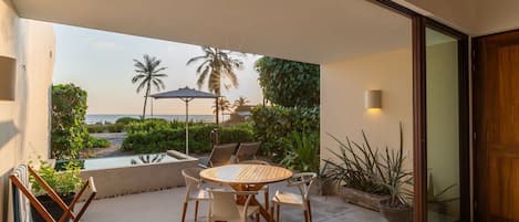 Une terrasse avec une table ronde et des chaises, une petite piscine et une vue sur l’océan et les palmiers.
