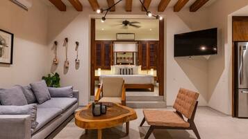 A modern living room with a sofa, a wooden coffee table, and a cushioned chair. A television is mounted on the wall, and a ceiling fan is visible.