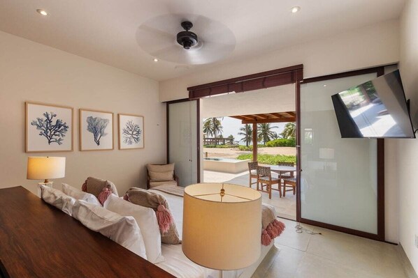 A modern hotel room with a bed, a sofa, a TV, and a view of the outdoor pool area.
