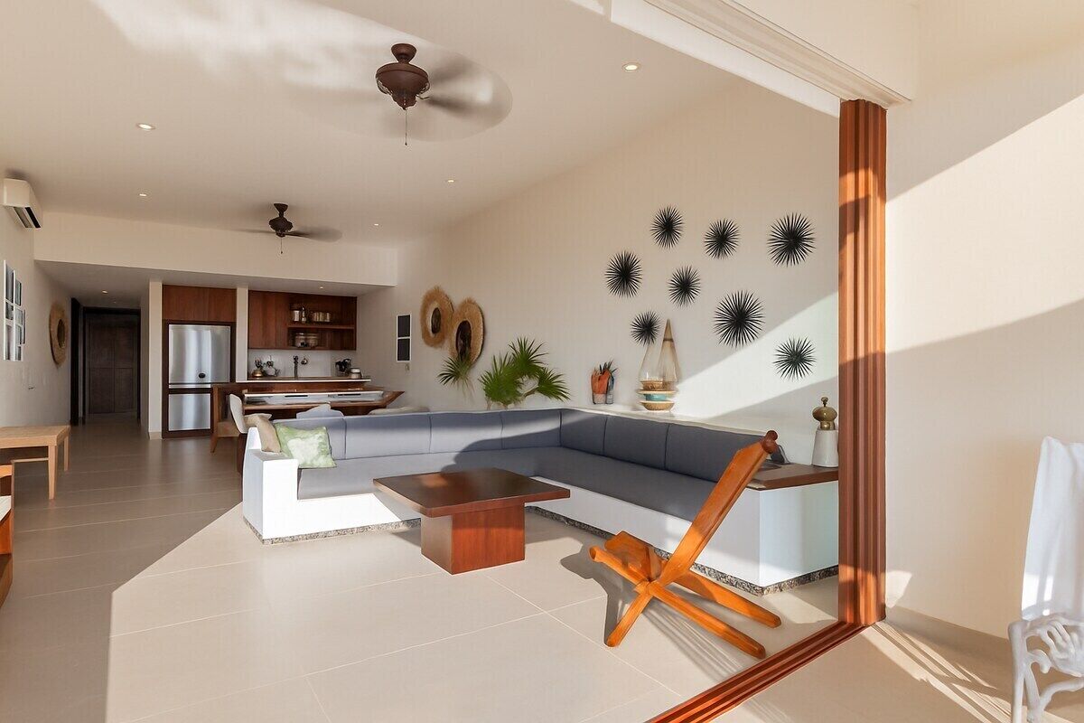 Un salon moderne avec un canapé d’angle, une table basse et un coin repas agrémenté d’une chaise en bois.