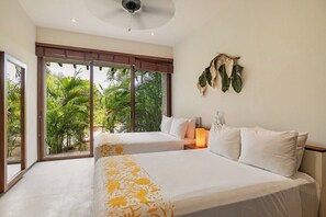 A hotel room with two beds, a ceiling fan, a large window with a view of greenery, and a wall-mounted decoration. - 3BR Villa I Steps to Playa Blanca + Pool (Zihuatanejo)