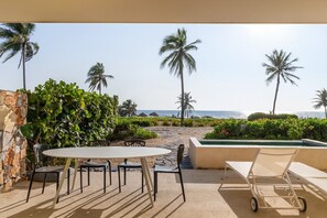 A patio with a table and chairs, a pool, and a view of the beach and ocean.