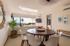 A modern dining area with a round table, white chairs, a potted plant, and a view of the outdoors. - 3BR Villa I Steps to Playa Blanca + Pool (Zihuatanejo)