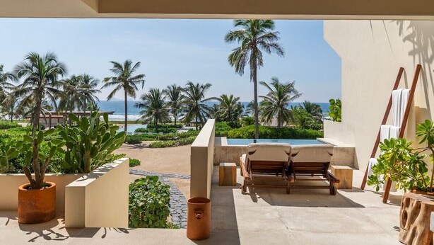 A poolside area with a view of the ocean, palm trees, and a wooden lounge chair. - Zihuatanejo 3BR • Sunset Views, Pool + Beach Acces (Zihuatanejo)
