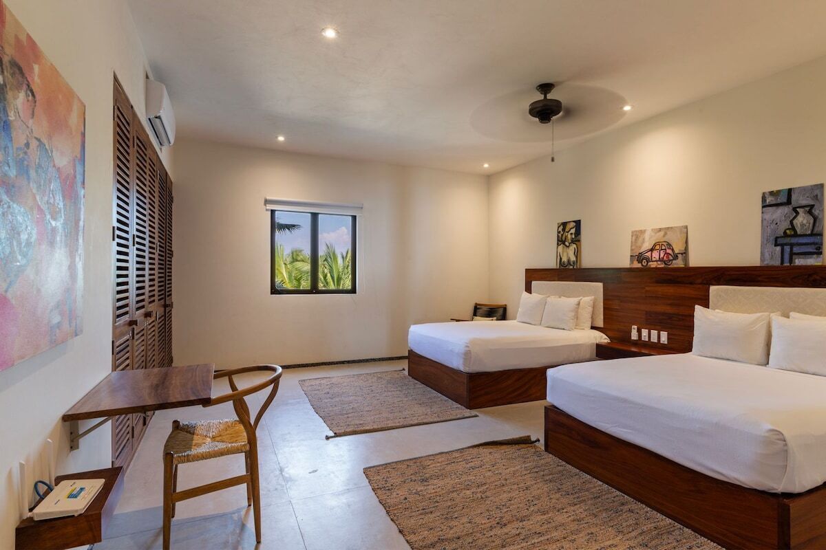 Une chambre d’hôtel avec un lit, un bureau et une chaise. Il y a une fenêtre donnant sur des palmiers.
